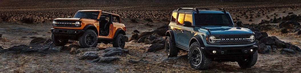 Ford Bronco and Ford Bronco Sport parked in the desert during sunset