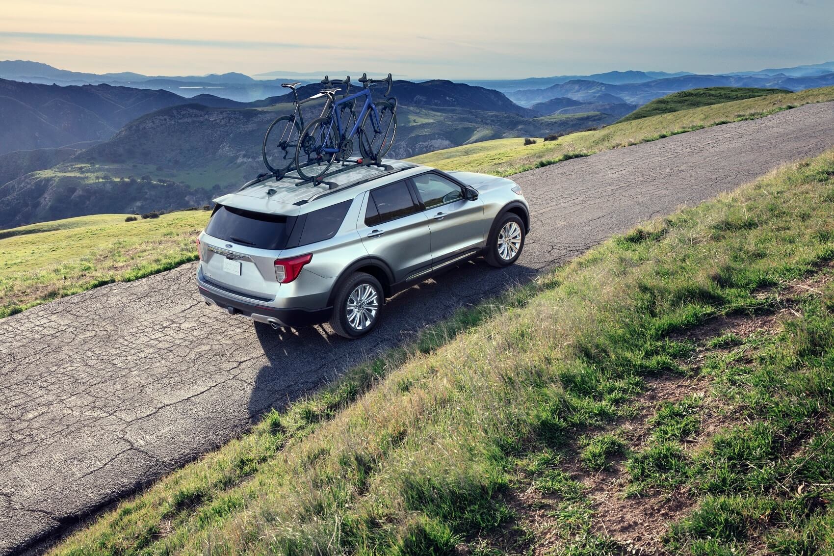 Used Ford Explorer driving on scenic mountain road with bikes on top of car
