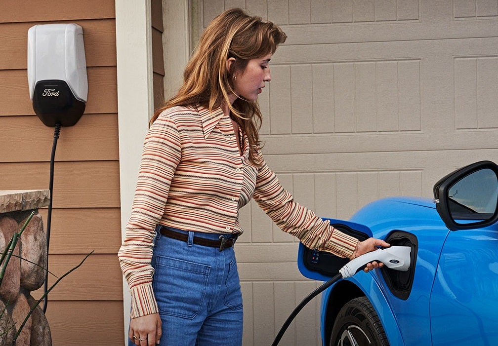 Woman plugging in charger to Ford Mustang Mach-E using home charging station